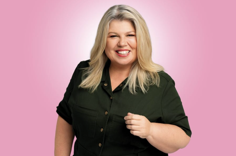 Portrait of comedian Urzila Carlson smiling in a green top against a pink background.